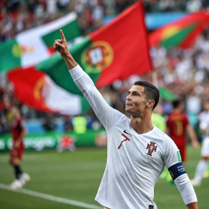 Cristiano Ronaldo, Portuguese soccer player, posing with arm raised. Soccer field blurred in background, only crowd visible.