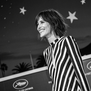 Katherine Moennig, actress, smiling at the Cannes Film Festival. Black and white striped dress, dark sky backdrop