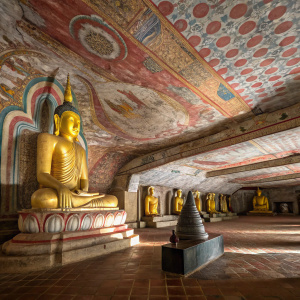 Dambulla Cave Temple, Sri Lanka. UNESCO World Heritage Site. Vibrant paintings and sculptures adorn walls. Large golden Buddha statue in meditation, surrounded by smaller Buddhas. Intricate ceiling paintings.