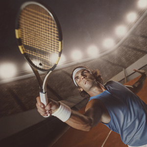 Rafael Nadal in animated style, mid-swing with tennis racket. Intense expression, blue attire. Stadium lights casting shadows in night scene.
