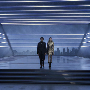 Riccardo Pozzoli, Chiara Ferragni at Louis Vuitton Fashion Show. Riccardo in black suit, Chiara in glamorous gold dress. Neon lit cityscape backdrop