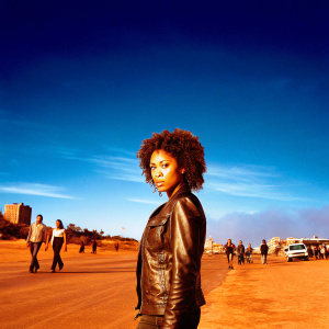Annie Ilonzeh, actor from General Hospital, intense gaze, curly hair, black leather jacket, standing in a bustling city street.