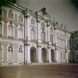 Vintage black and white photo of the Winter Palace in St. Petersburg. Grand building with intricate details, sculptures, and ornate window frames. Slightly angled perspective, highlighting the grandeur and symmetry.