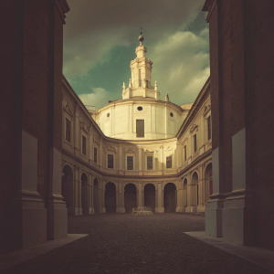 Stunning late afternoon shot of Francesco Borromini's Church of Sant'Ivo alla Sapienza. Roman Baroque masterpiece. Golden hues of the facade, contrasting blue sky and white clouds. Cobblestone courtyard