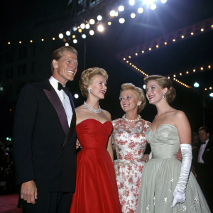 Dan Duryea, Jan Sterling, Patty McCormack, and Mary Fickett at a vintage Hollywood gala. They are dressed in elegant 1950s attire. Bright stage lights, glamorous setting.
