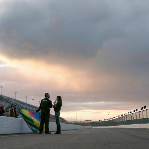 Matt Kenseth and Danica Patrick chatting beside a colorful banner. Crowds and track visible in the background.
