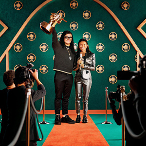 Skrillex and Sirah accepting an award at the MTV Video Music Awards. Golden trophy on stage. Red carpet event