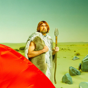 Actor portraying prehistoric character in 'Korg: 70,000 BC'. Desert setting with rocky terrain. Fur outfit and stone weapon. Intense gaze.