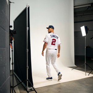 Andrelton Simmons, wearing a white jersey with his name and number, stepping into a photo shoot in a sleek studio. No crowd, modern backdrop