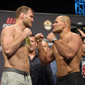 Stipe Miocic and Junior Dos Santos, shirtless and in boxing stance, at a UFC weigh-in event.