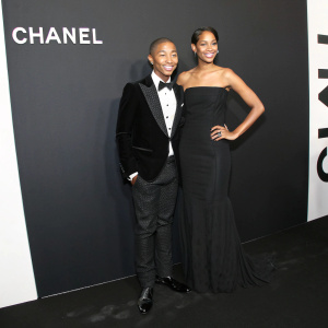 Pharrell Williams and Helen Lasichanh attending a luxury fashion gala. Stark black and white backdrop, adorned with Chanel logos.
