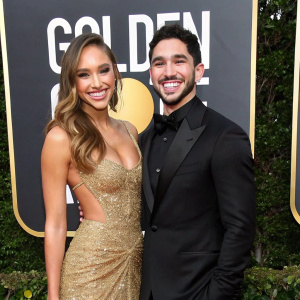 Alexis Ren and Alan Bersten, beaming at the Golden Globe Awards. Black and gold themed backdrop with star logos.