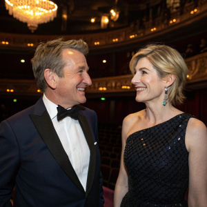 Bradley Walsh and Jodie Whittaker, elegantly dressed, smiling and chatting at BAFTA's annual ceremony. Luxurious venue, dim lighting