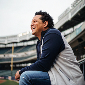 Miguel Cabrera in a candid moment. Dark curly hair, joyful expression. Poses in casual attire outside a stadium.