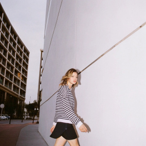 Jennifer Lawrence, casually dressed in a black and white striped sweater and a black skirt, walks down a busy urban street. A modern building with sleek windows and an urban backdrop provide the setting.