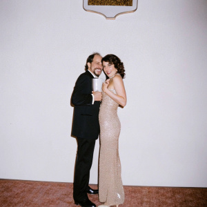 Richard Schiff and Lisa Edelstein at the Emmy Awards, posing in front of the Hollywood sign. Richard in a black suit, Lisa in a gold sequined dress.