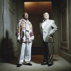 Jacob Zuma and Sepp Blatter attending a gala dinner. Jacob in vibrant traditional attire, Sepp in sharp business suit.