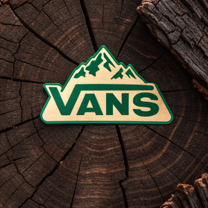 Creative design featuring the VANS logo. Mountain-like shape, green color. Dark brown, rough wooden backdrop, enhancing the rugged texture. Eye-catching, memorable, unique, simple, impactful, clear, recognizable brand identity.