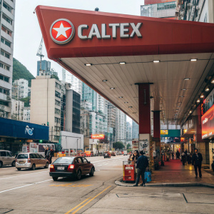 Large red awning with Caltex logo over Hong Kong street. Vehicles refueling, advertisements, and construction cranes visible.