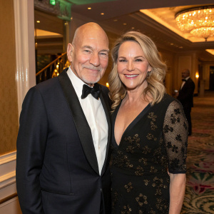 Patrick Stewart and Wendy Neuss at the star-studded gala. They are posing with warm smiles indoors, surrounded by elegant decor.