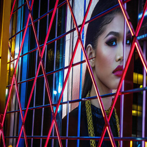Zendaya, singer and actress, in a dramatic red carpet look. Her makeup is bold and dramatic, with a focus on her eye shadow and lip color. Wearing a gold chain necklace. Against a black backdrop.