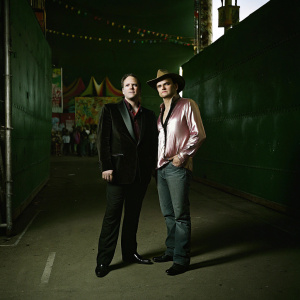 Quentin Tarantino and Robert Rodriguez at a film festival. They stand together in front of a backdrop filled with sponsor logos. The event setting is vibrant and bustling.