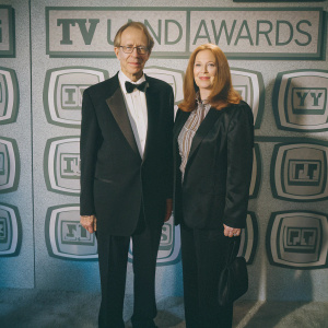 Bernie Kopell and Catrina Honadle at the TV Land Awards. They are dressed in formal attire, Bernie in a black tuxedo and bow-tie, Catrina in a black blazer and pants. The backdrop is plain white with TV Land Awards logos.