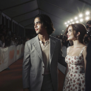 Avan Jogia and Zoey Deutch, dressed to impress, attending the annual Nickelodeon's Kids' Choice Awards. Avan in a gray suit and beige shirt, Zoey in a floral dress. Crowded red carpet scene.