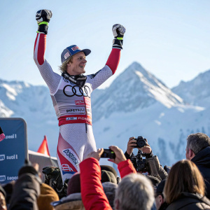 Henrik Kristoffersen on the podium after winning a gold medal at the Audi FIS Alpine Ski World Cup. Crowds cheering, snow covered mountains in the background.