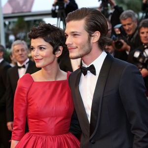Audrey Tautou and Gaspard Ulliel attending a glamorous film premiere. Audrey in a vibrant red dress. Gaspard in a sleek tuxedo. Crowded, star-studded red carpet event.