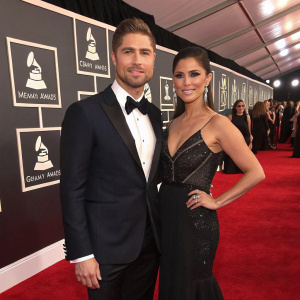 Eric Winter and Rosalyn Sanchez at the Grammy Awards ceremony. They wear formal attire. Red carpet with grammy logos in background