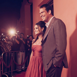 Mila Kunis and Scott Stuber, attending a Hollywood movie premiere. Bright lights and paparazzi flashes.