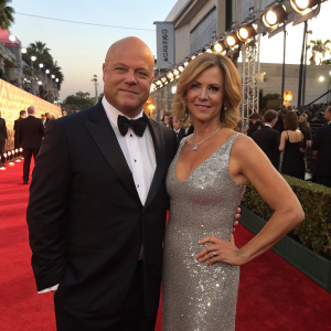 Michael Chiklis and Michelle Moran at a glamorous awards show. Both are on the red carpet, Michael in a tuxedo, Michelle in a sparkling silver dress.