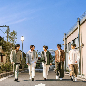 SHINee members, Onew, Key, Minho, Taemin, and Luhan, in casual attire, walking down a busy street in Seoul. The vibrant cityscape and bright lights serve as the backdrop.