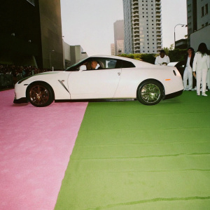 A sleek Nissan GT-R35 parked on a bustling city street. Crowds of people and tall buildings in the background