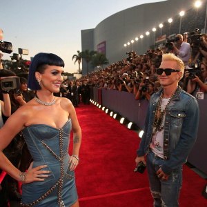 Katy Perry and Riff Raff at VMAs. Katy in a sparkling dress, Riff Raff in denim and chains. Crowded red carpet with flashing cameras.