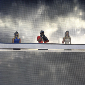 Ne-Yo, JoJo, and Kristin Cavallari on the Teen Choice Awards stage. Ne-Yo in a vibrant outfit, sunglasses, and cap. JoJo in blue dress, relaxed hairstyle. Kristin Cavallari with blonde hair, patterned dress. Stage with pixelated backdrop.