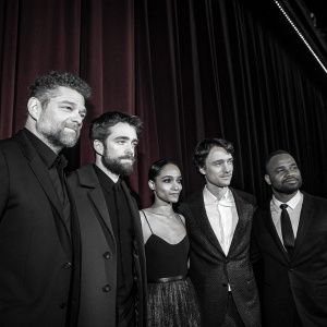 Andy Serkis, Robert Pattinson, Zoë Kravitz, Paul Dano, and Jeffrey Wright at a VIP movie premiere. Black and white photography. Dark theater with red curtains backdrop
