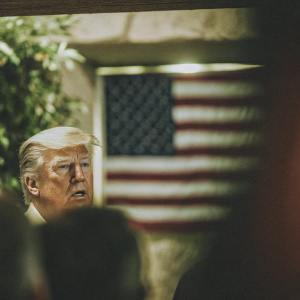 Close-up of Donald Trump, Caucasian male, older adult, blonde hair, standing in front of blurred American flag.
