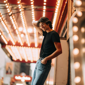 Grant Gustin, actor from The Flash, dressed casually in a black t-shirt and blue jeans. Poses in front of Times Square neon lights.