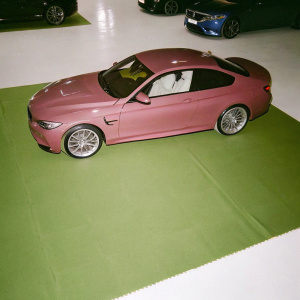 Luxury car showroom. Shiny red BMW M4 parked prominently. Sleek design highlighted. Brightly lit, spotless floor.