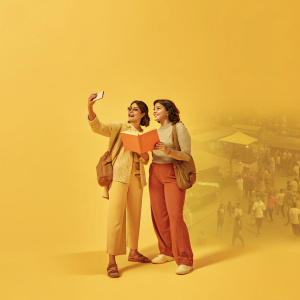 Gul Panag and Isha Koppikar in casual attire, attending an outdoor book launch event. Crowd and street scene in background.