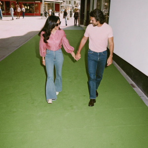 Eva Longoria and Jose Baston, dressed in casual outfits, walking down a bustling city street. Crowd of people around them.