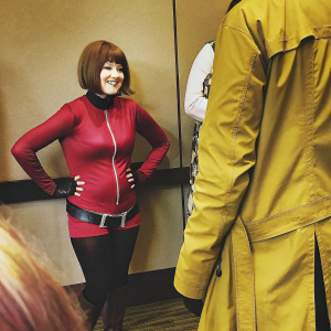 Ochako Uraraka from Boku no Hero Academia, with short brown hair and a close-fitting red top, standing against a white backdrop at a comic con.