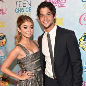 Sarah Hyland and Tyler Posey posing at an award show. Crowded backdrop filled with vibrant Teen Choice Awards logos. Close-up shot
