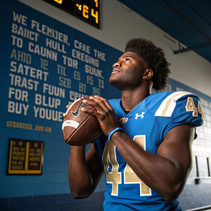 Myles Jack, football player, intense focus on the gridiron. He's clad in a blue jersey with number 44, no helmet, posing in a sports studio with motivational quotes on the walls.