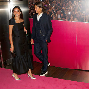Courtney Eaton and Brenton Thwaites, in elegant attire, pose at a bustling gala. Courtney in a sleek black gown and silver heels. Brenton in a sharp navy suit. Crowds of excited fans and paparazzi captured in the background.
