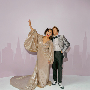 Sandra Oh and Andy Samberg at the Met Gala. Sandra in a shimmering gold gown, Andy in a black suit with a bow tie. They pose against a backdrop of NYC skyline.