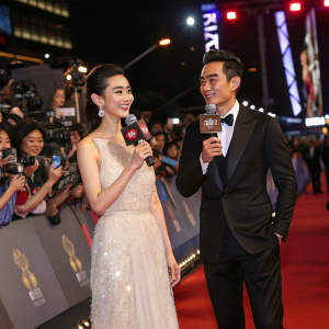 Angelababy and Eddie Peng, holding microphones, at a glamorous movie premiere. Crowded red carpet with flashing cameras.