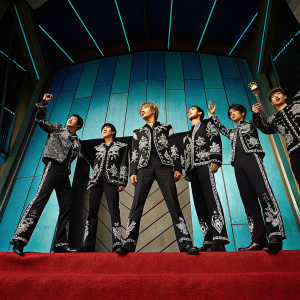 NCT Dream members on a vibrant red carpet. Gaon Chart Music Awards event. Colorful backdrop, black and white outfits with intricate embroidery. Dynamic poses and expressions.